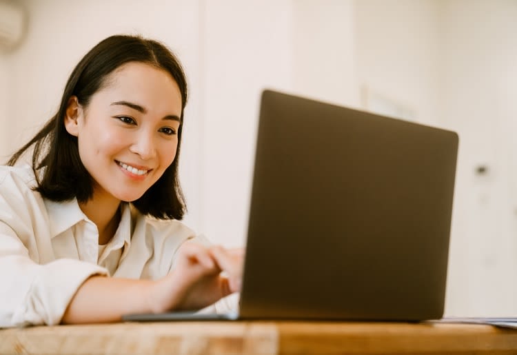 A young Asian woman smiling at her laptop screen