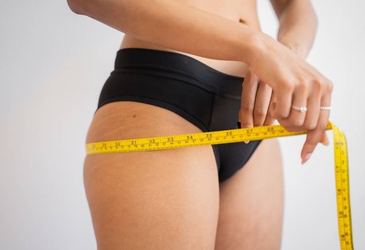 A woman uses a measuring tape to check her weight loss