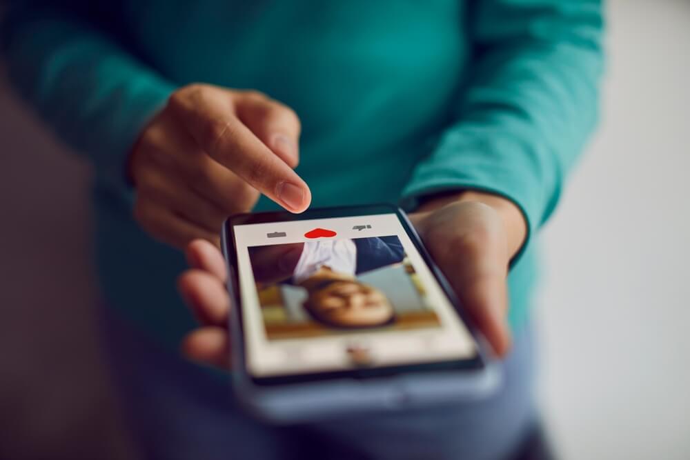 Dating online. Mobile phone in hands of woman who scrolling through profiles of men and pressing red heart button with her finger. 