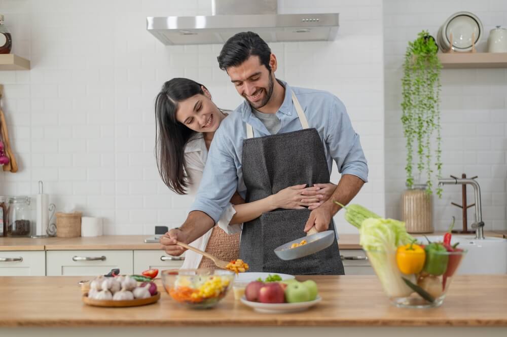 Happy couple in love cooking in the kitchen counter at home and hugging