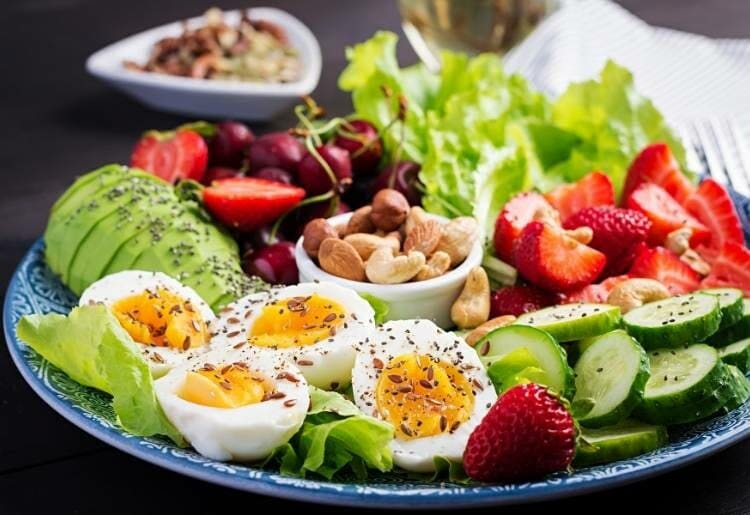 A plate of paleo-friendly food, including eggs, avocado, cucumber, lettuce, and strawberries