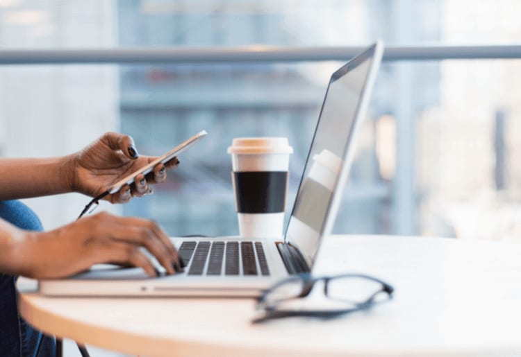 Woman holding phone and working on laptop