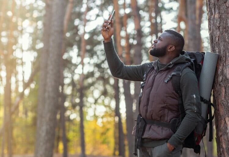 A man standing in the woods taking a selfie with his cell phone.