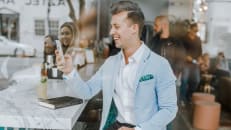 A young man smiles at his phone in a busy cafe