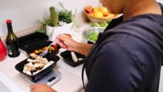 An woman portions off food with the help of a food scale to track her macronutrients