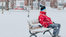 A man with depression sits alone on a bench in winter surrounded by snow