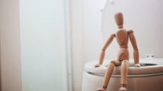 A wooden jointed doll sits on the toilet