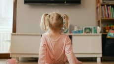 Portrait of happy baby playing with toys and watches cartoons on TV in playroom.