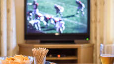 Watching American football match on TV with snacks and alcohol