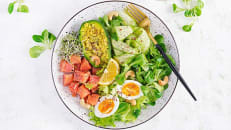 A healthy bowl of salad with avocado, eggs, and tomato.