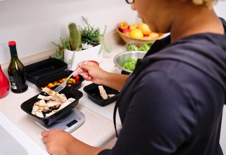 An woman portions off food with the help of a food scale to track her macronutrients