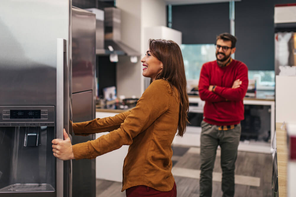 Young couple, satisfied customers choosing fridges in appliances store.