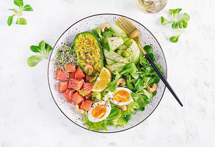 A healthy bowl of salad with avocado, eggs, and tomato.